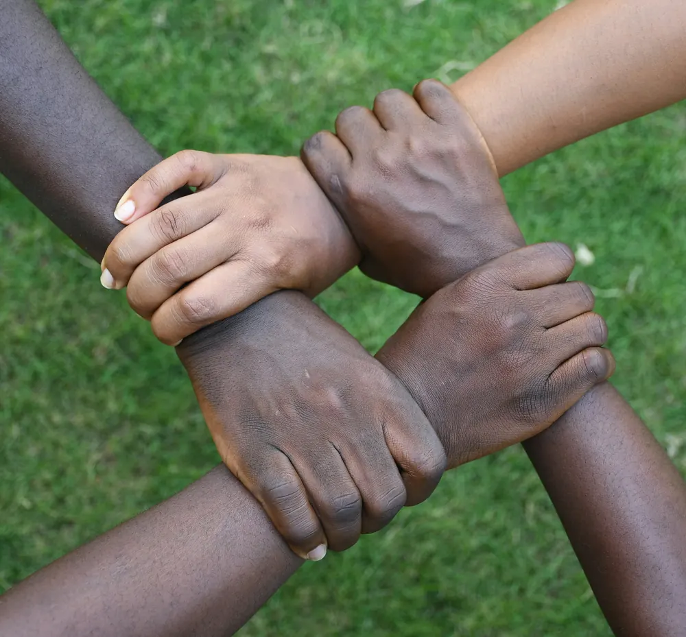 Four hands linked together in a square over green grass