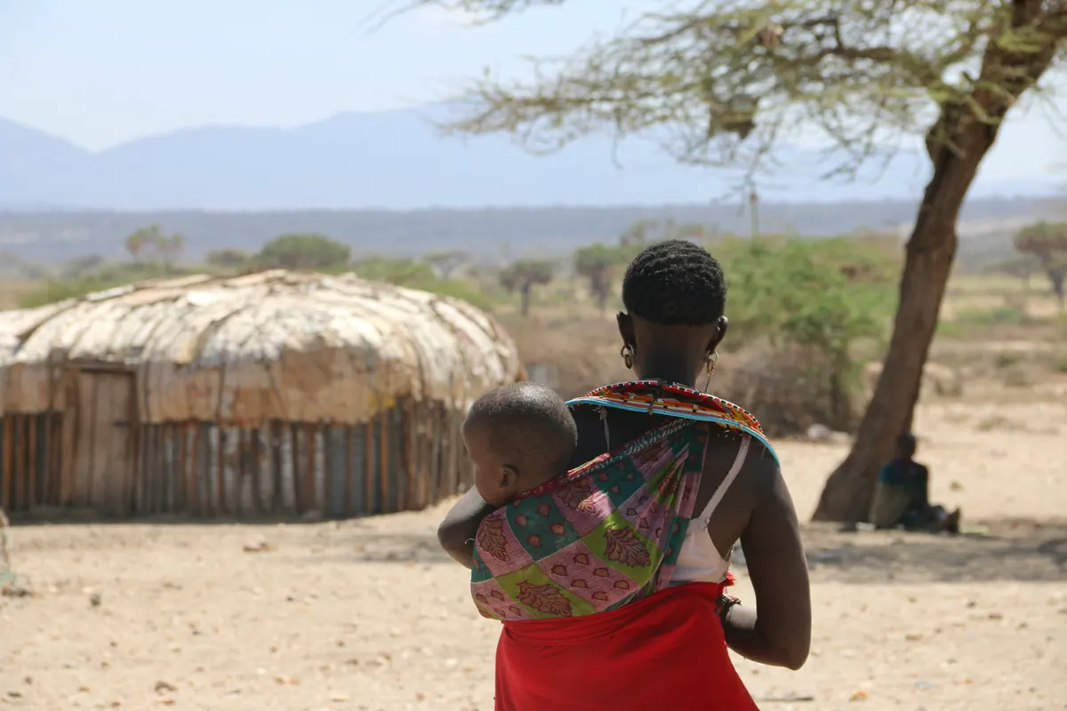 A mother carrying her baby on her back in a rural village
