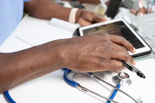 A clinician with a stethoscope reviewing notes on a tablet